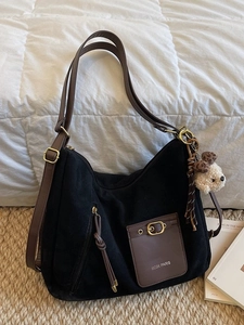 Grand sac fourre-tout noir avec poche marron et charm peluche chien sur un lit