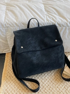 Minimalist black matte leather flap backpack with silver metal buttons in a cozy home setting