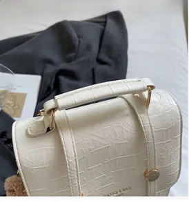 Close-up of cream crocodile pattern handbag with sturdy handle and gold hardware detail