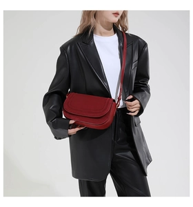 Detail of a dark red matte leather saddle bag worn over a black leather blazer