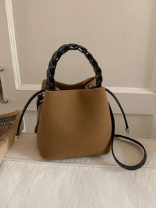 Brown wool bucket bag with black woven handle and crossbody strap in elegant setting