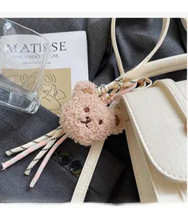 Close-up of a pink plush bear charm in lamb wool on a white textured flap handbag