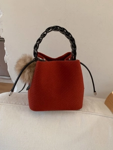 Red woven bucket bag with black braided handle and brown fur ball charm detail