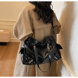 Detail view of large black shiny tote bag with silver studs and buckles on a model