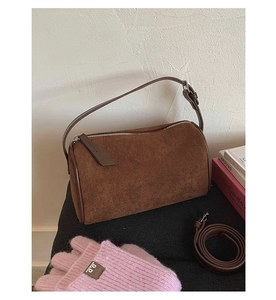 Detail view of a brown suede cylinder bag with leather straps on a dark surface