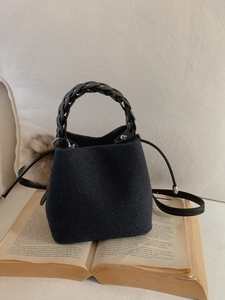Dark blue felt bucket bag with black woven handle and brown fur pompom charm on open book