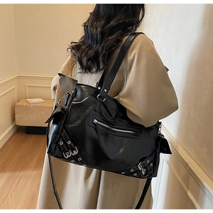 Detail of black glossy tote bag with metal buckles and straps worn with a khaki trench coat