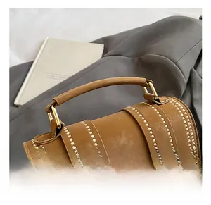 Detail der braunen Zylindertasche mit Goldnieten und metallischem Drehverschluss