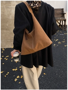 Brown suede hobo bag with contrast stitching and tassels in an autumn street setting