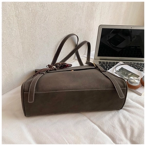 Detail of dark brown leather tote bag with contrast stitching and decorative tassel on desk