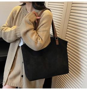 Detail of a large black suede tote bag with brown straps worn on a beige cardigan