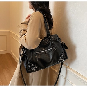 Detail of a large black leather tote bag with metallic studs on a stylish trench coat