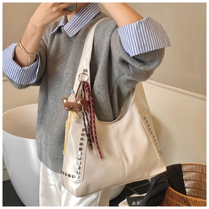 Detail of a large cream hobo tote bag with silver studs and a cute brown bear charm