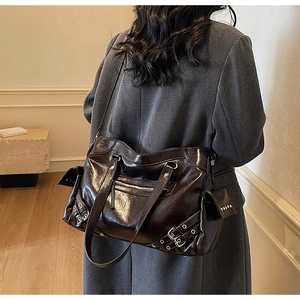 Detail of dark brown glossy patent leather tote bag with silver hardware on a model