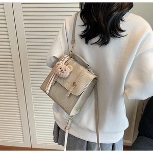 Dettaglio borsa beige con trama a coccodrillo, ciondolo a orsetto e foulard di seta