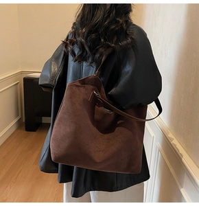 Close-up of a minimalist dark brown suede tote bag carried by a model in a modern interior