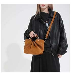 Detail of tan bucket bag with gold ring handle and adjustable shoulder strap on model