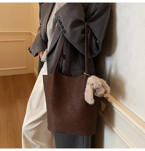 Detail of dark brown woven tote bag with plush bunny charm on a casual work outfit
