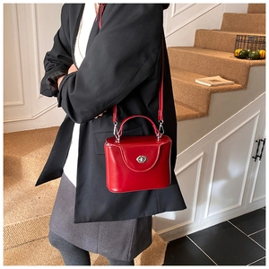 Sac boîte chic en similicuir rouge assorti à un manteau noir dans un escalier