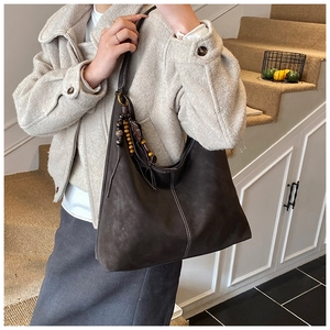 Detail of dark brown matte leather tote bag featuring ethnic wood bead charm and white stitching