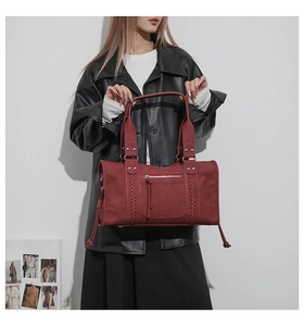 Close-up of a burgundy fashion travel bag with metallic rivets and woven side details
