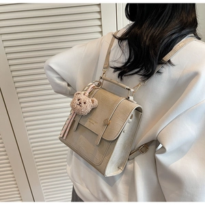 Dettaglio dello zaino beige motivo coccodrillo con ciondolo a forma di orso bruno