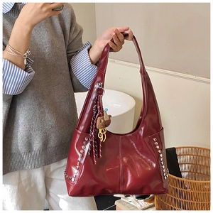 Detail of dark red tote bag featuring glossy leather, silver rivets and a bear charm