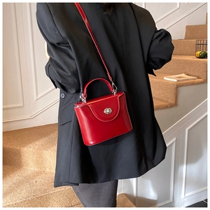 Sac à main vintage rouge avec fermoir métallique porté sur un blazer noir élégant