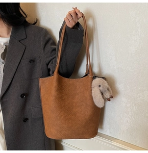 Detail of woven brown tote bag with plush bunny charm on gray suit model