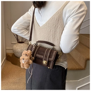 Detail der braunen Boston-Tasche aus Wildleder mit Goldnieten und Plüschbären-Anhänger