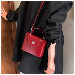 Détail d'un petit sac boîte rouge brillant avec fermoir rotatif argenté sur veste noire