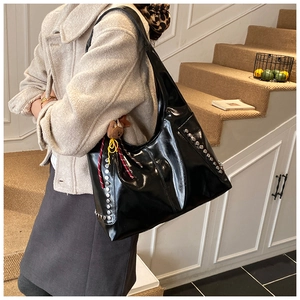 Detail of glossy black tote bag with metal rivet studs and cute bear pendant accessory
