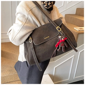 Detail of vintage brown leather tote bag featuring golden logo and cute bear pendant charm