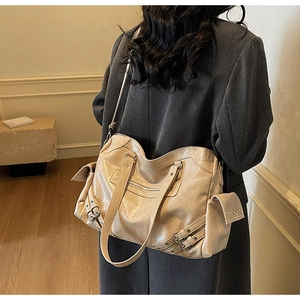 Detail of a large beige leather tote bag with retro buckles and zipper design