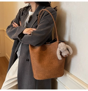 Detail of dark brown woven tote bag with plush rabbit pendant on model's shoulder