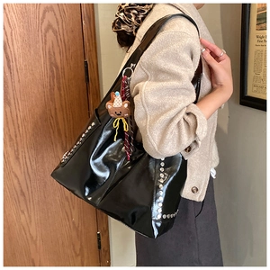 Macro detail of black glossy tote bag with silver studs and brown teddy bear charm