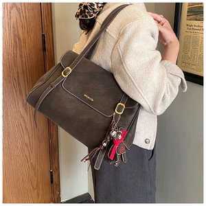 Detail of vintage brown tote bag with bear charm and golden logo on matte leather