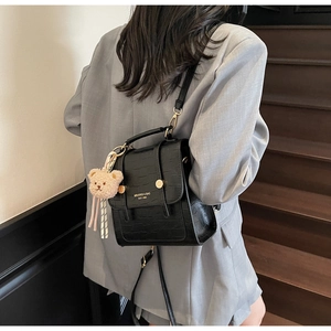 Detail of black crocodile texture mini backpack with cute teddy bear charm on model