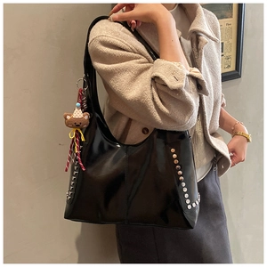 Detailed view of black patent leather hobo bag with silver studs and plush bear charm
