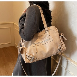 Detail view of large beige leather tote bag with rivets and shoulder strap on model
