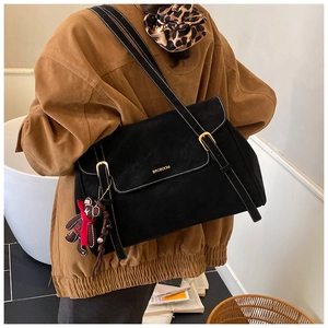Close-up of black suede shoulder bag with white stitching and bear charm detail