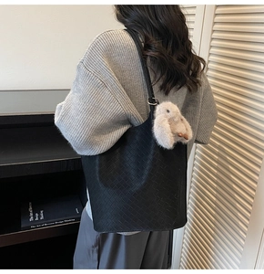 Detail of black woven leather tote bag with grey rabbit pendant on model in minimalist room