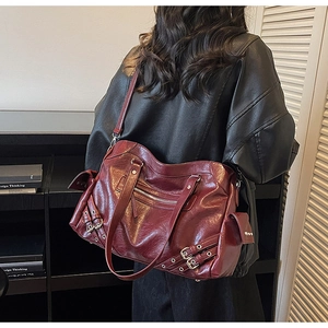 Detail of dark red faux leather tote bag with punk rivets and decorative belt buckles