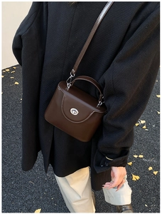 Gros plan sur sac bandoulière marron foncé avec fermoir rotatif argenté sur feuilles