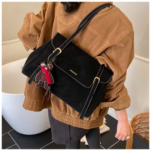 Detail of black suede messenger bag with gold logo and cute bear charm in lifestyle setting