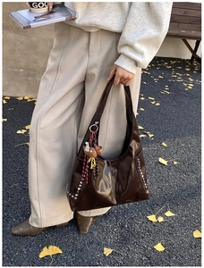 Close-up of brown oiled leather tote bag featuring silver studs and bear charm detail