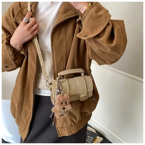 Dettaglio borsa beige con patta, chiusura girevole dorata e ciondolo a cucciolo