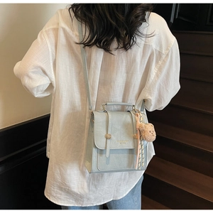 Detail of light blue crocodile texture bag with gold buckles and plush bear charm