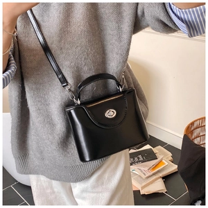 Sac trapèze noir chic avec fermoir rotatif argenté porté par un mannequin en gros plan