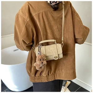 Dettaglio della borsa cilindrica beige con manico in metallo e ciondolo orsetto